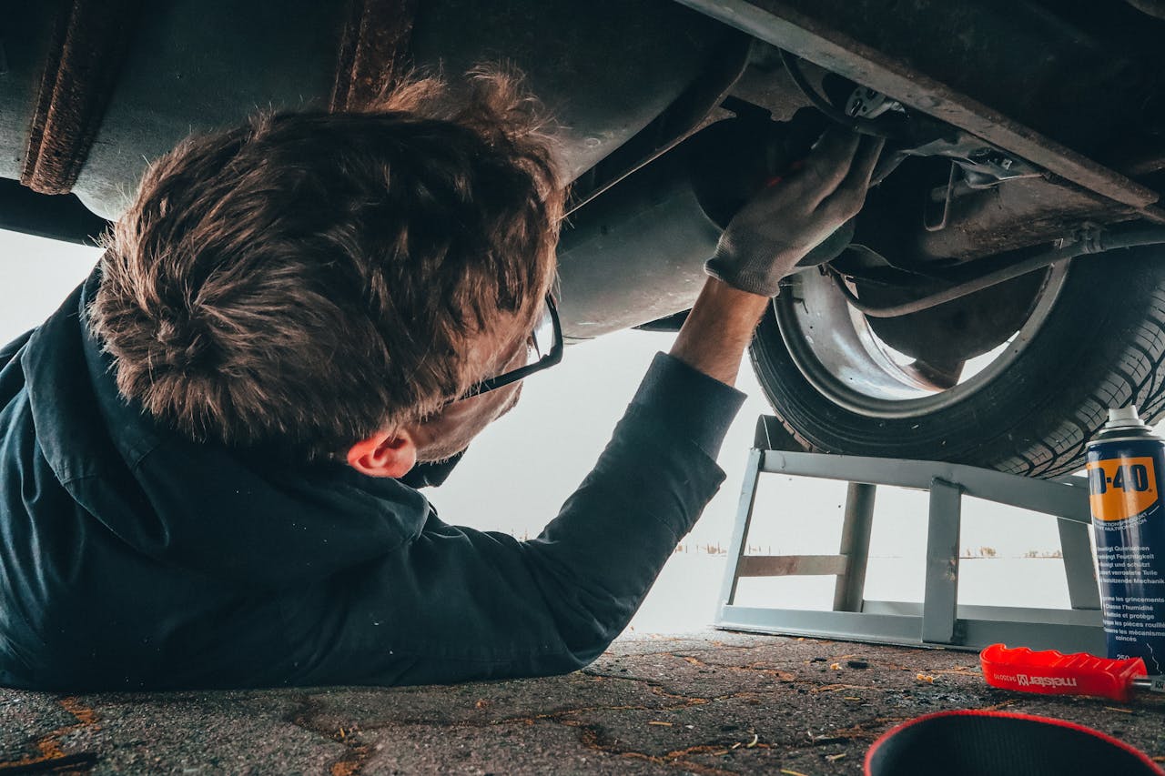 project-03-a Mechanic skillfully repairing car undercarriage in outdoor setting with tools.